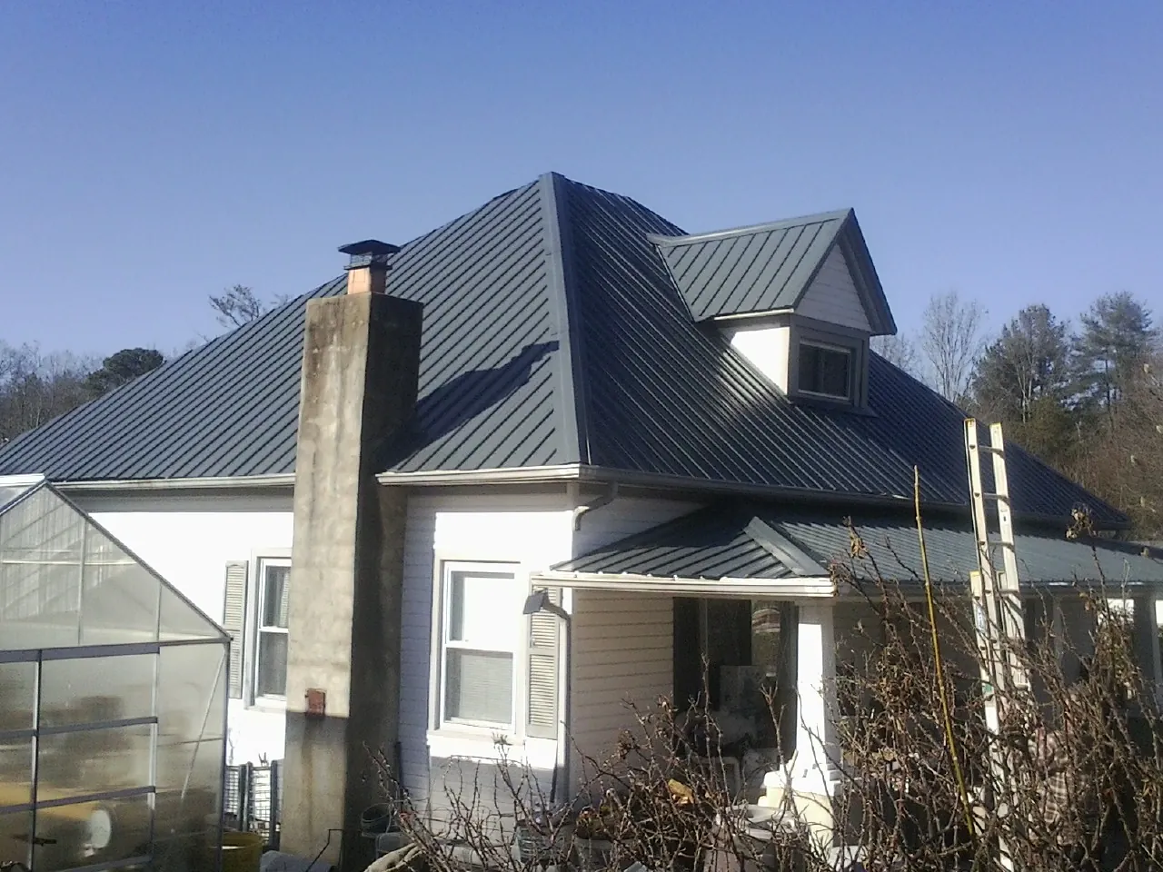 Dark blue standing seam metal roof on a white farmhouse with dormer — Slate & Tile Roof Repair by Roofing Brothers in Hurt