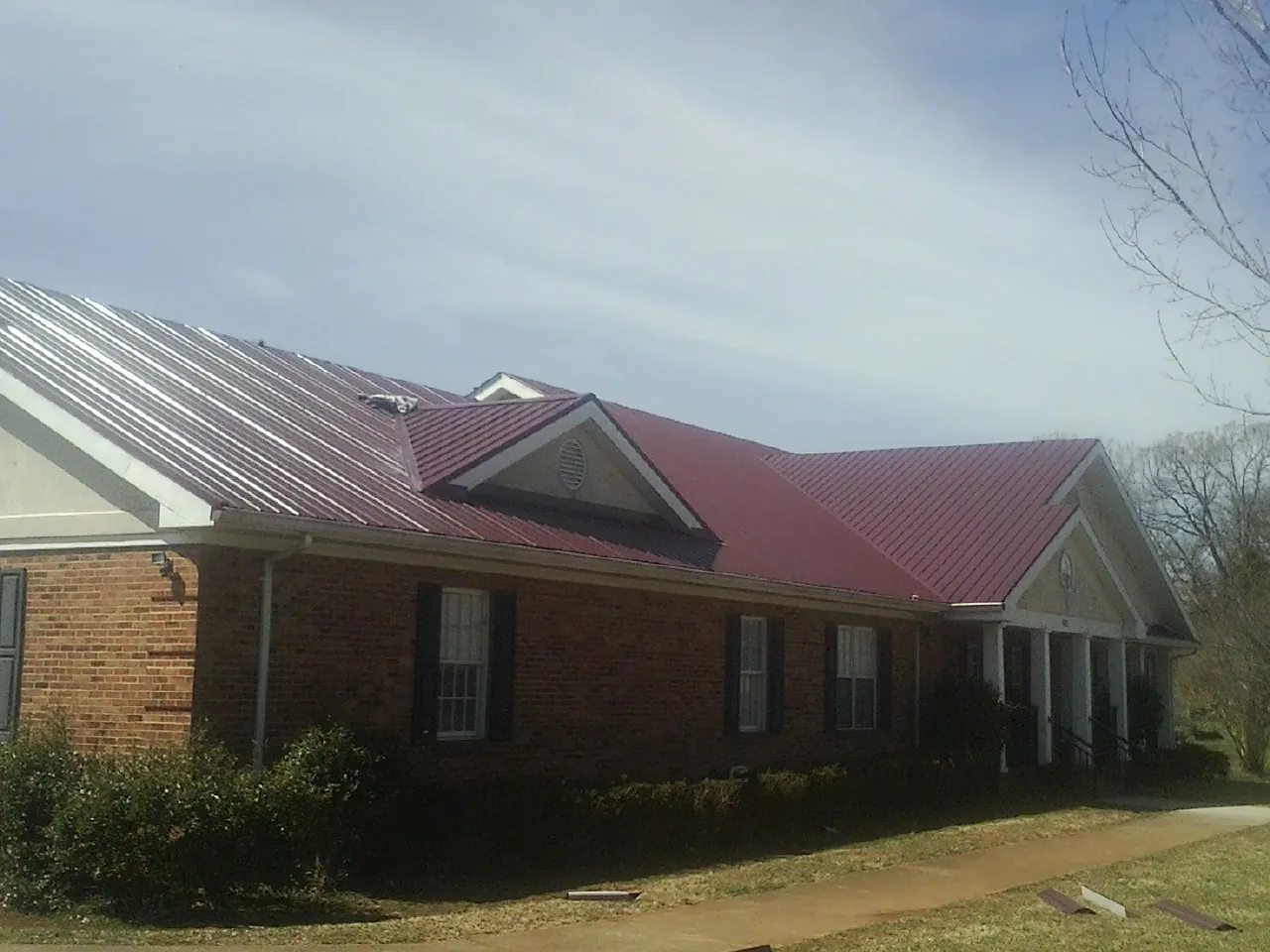 Red metal roof with gabled entries on a long brick building, from a Hail Damage Roof Repair job in Hurt