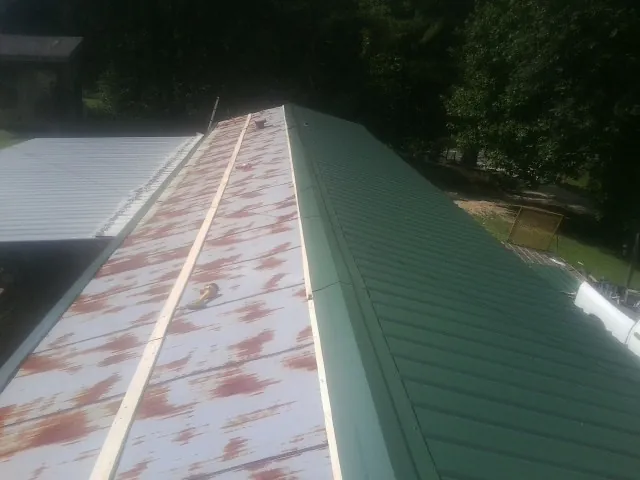 Old rusted panels beside newly installed green metal roofing — Wind Damage Roof Repair by Roofing Brothers in Hurt