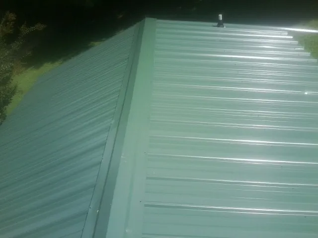 New green metal panels meeting at the ridge of a roof — Flat Roof Repair work by our crew in Hurt