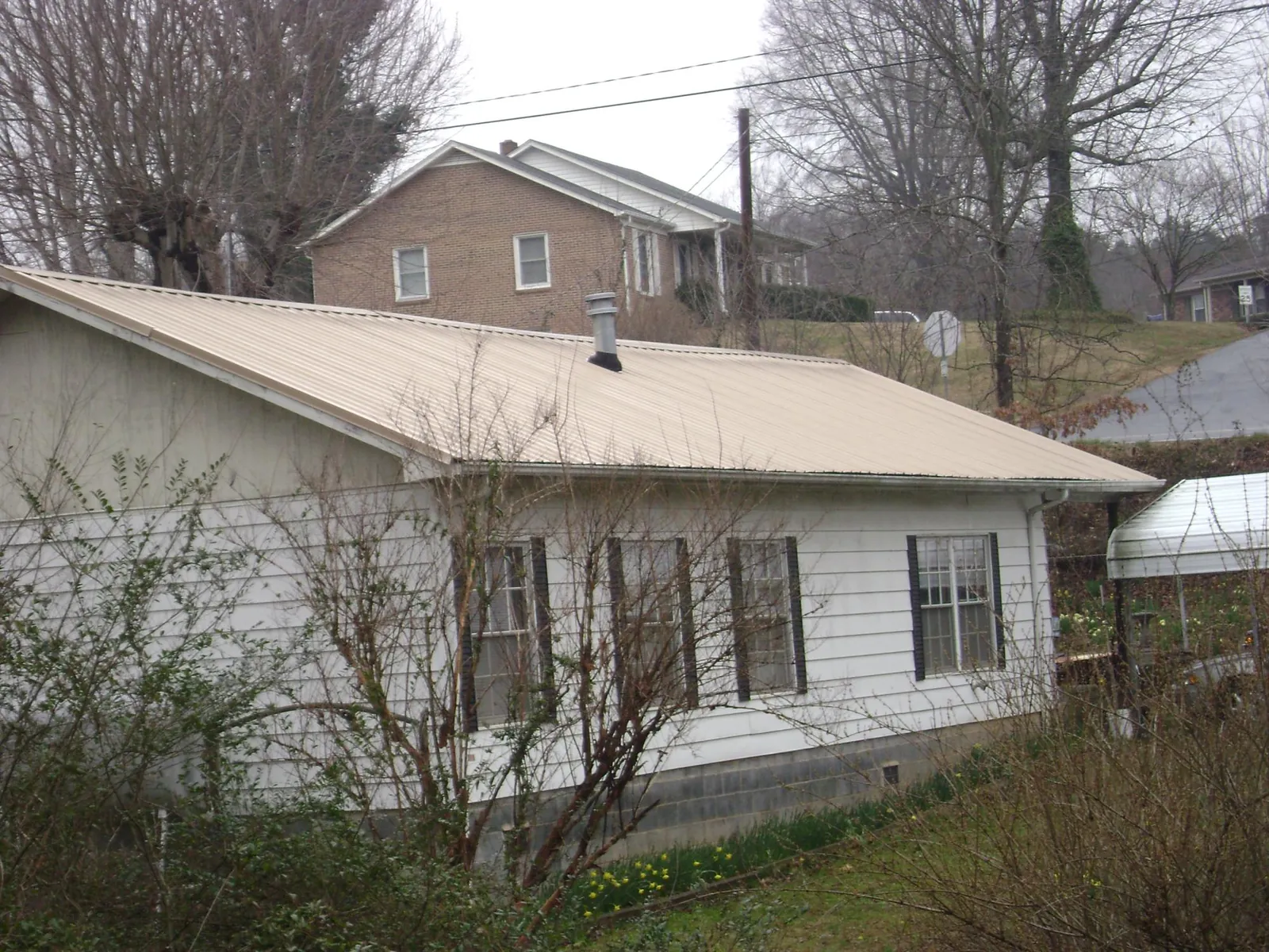 Tan metal roof on a white sided house set into a hillside — Commercial Roofing by Roofing Brothers in Hurt
