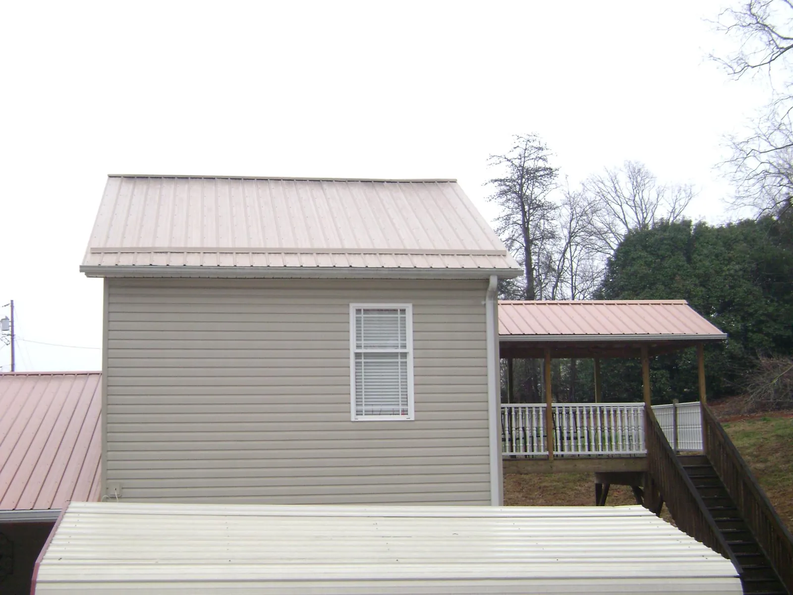 Tan metal roofs on a two story addition and attached porch, from a Roof Replacement job in Hurt